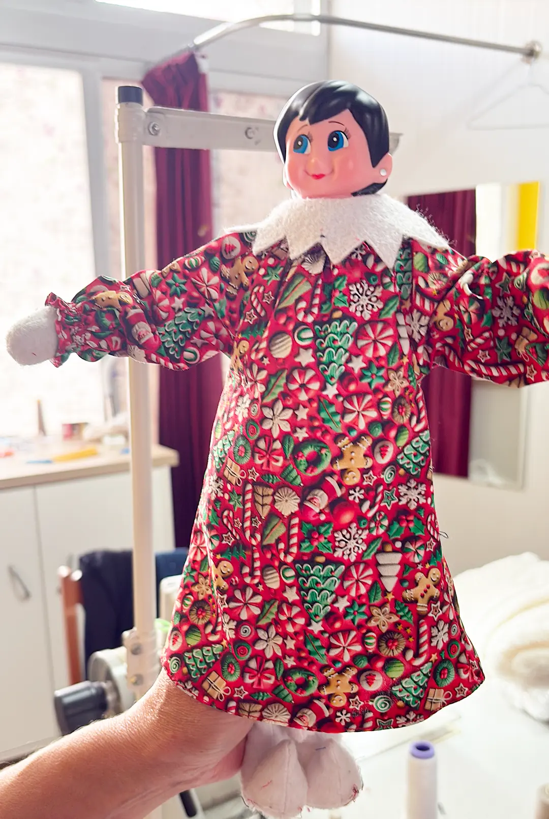 Un Lutin Farceur en robe de Noël, tenu à la main dans l’atelier de couture au Portugal